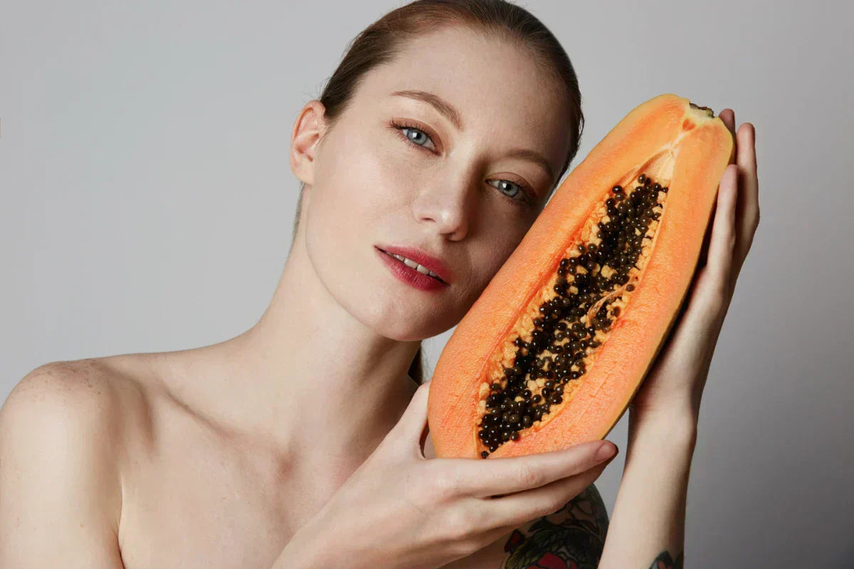 Woman holding a fresh papaya, highlighting the natural source of papain used in skincare products.